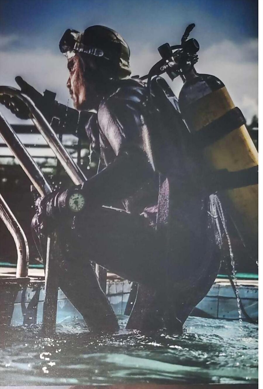 A combat diver in a wetsuit climbing from the water