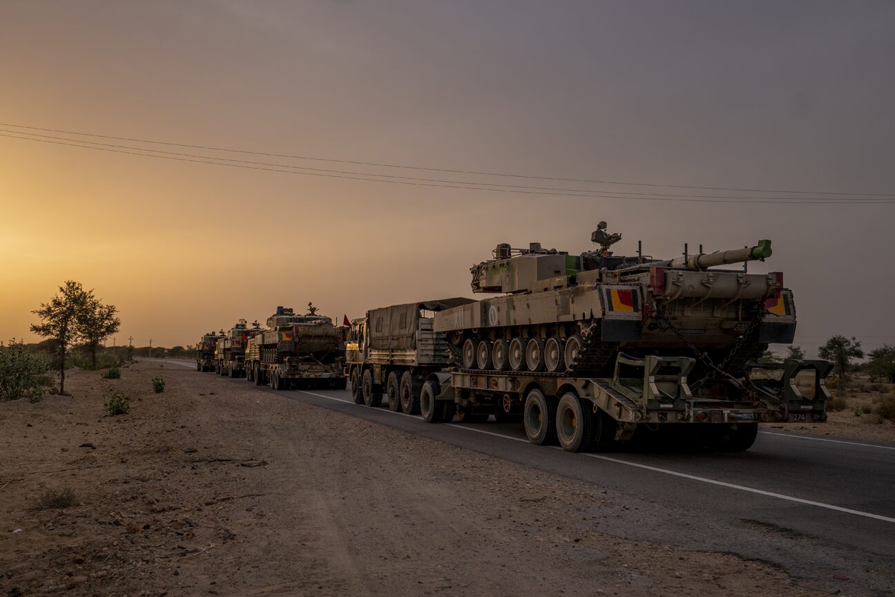 A column of tank transporters halted along a desert road at sunset