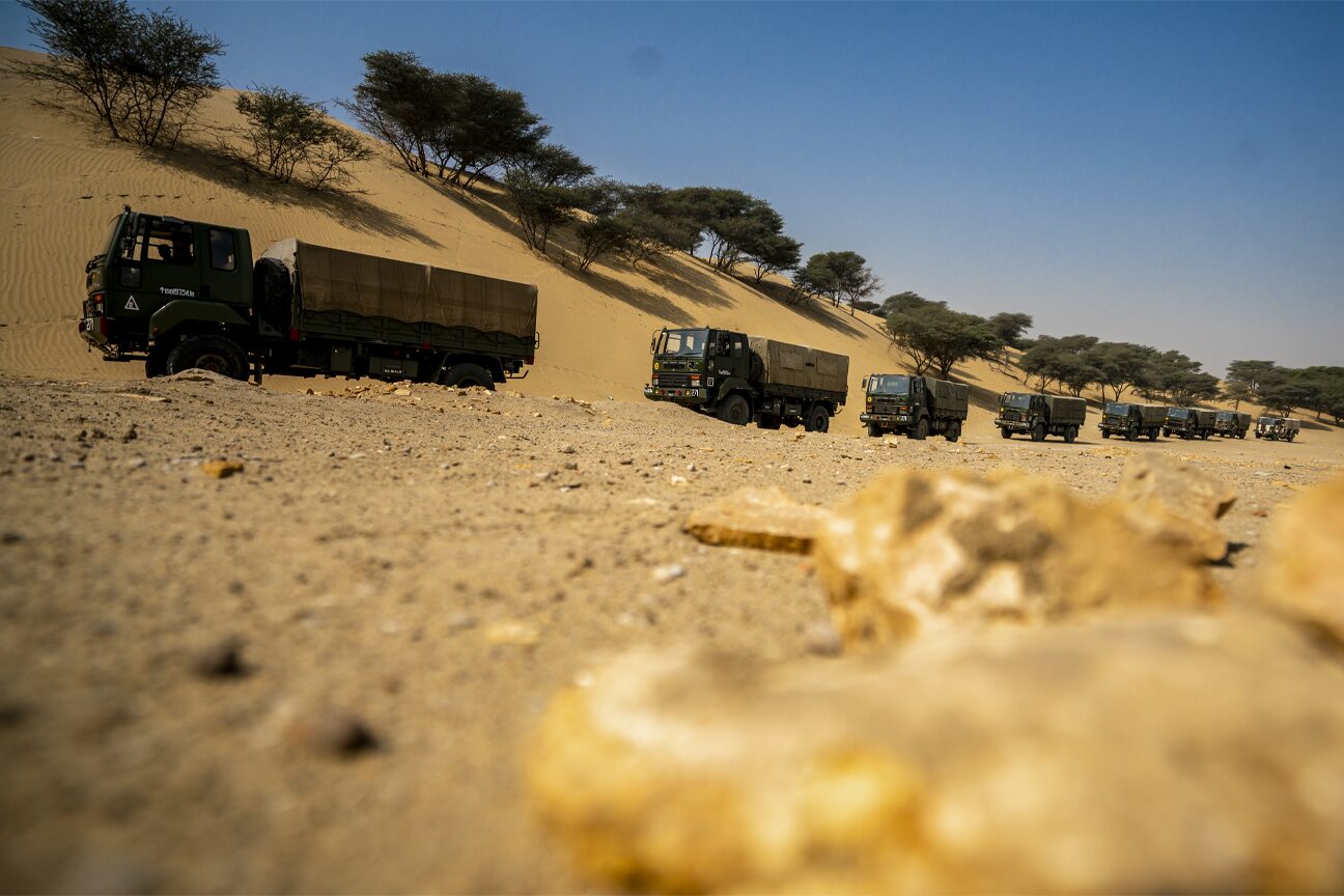 Army trucks harboured in line among desert dunes and thorn trees