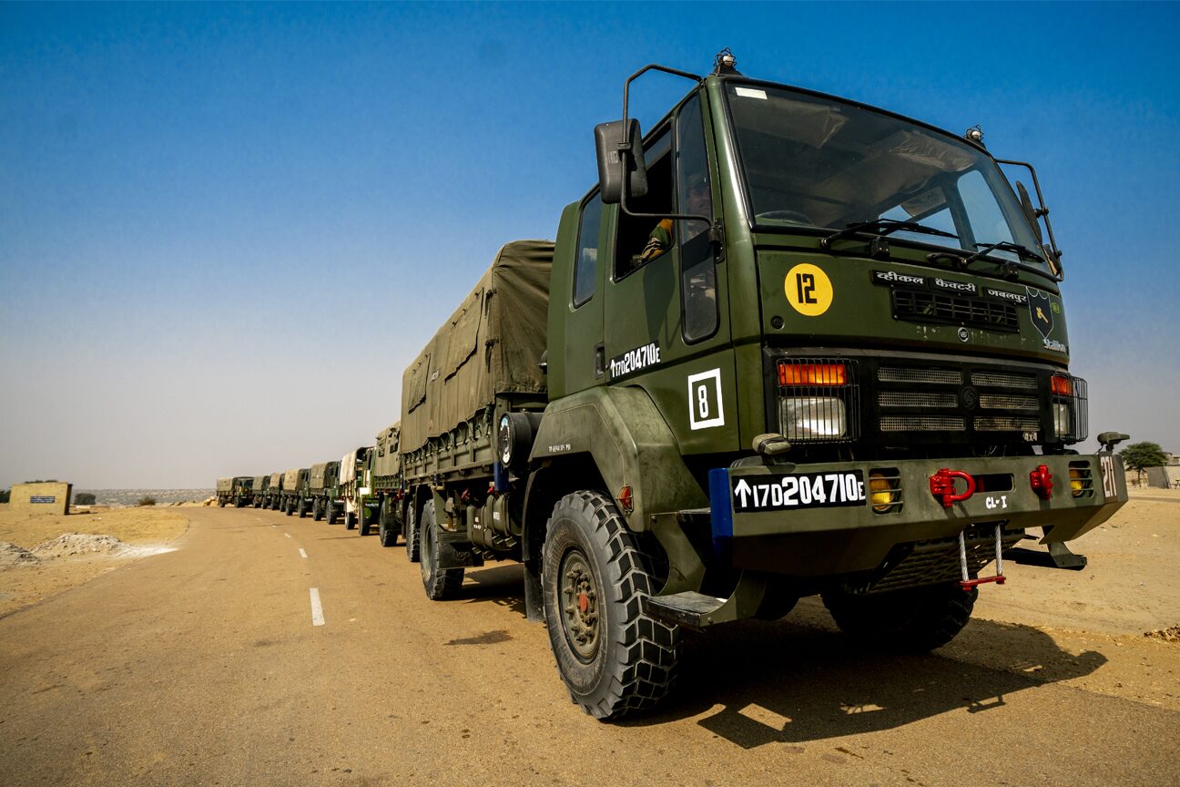 A column of Army trucks nose to tail on a desert road under a clear sky