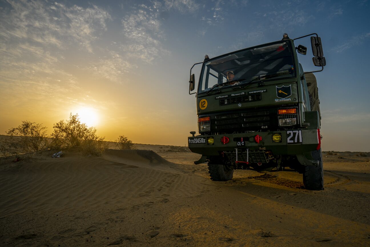 An Army truck standing on a dune with the sun low behind it