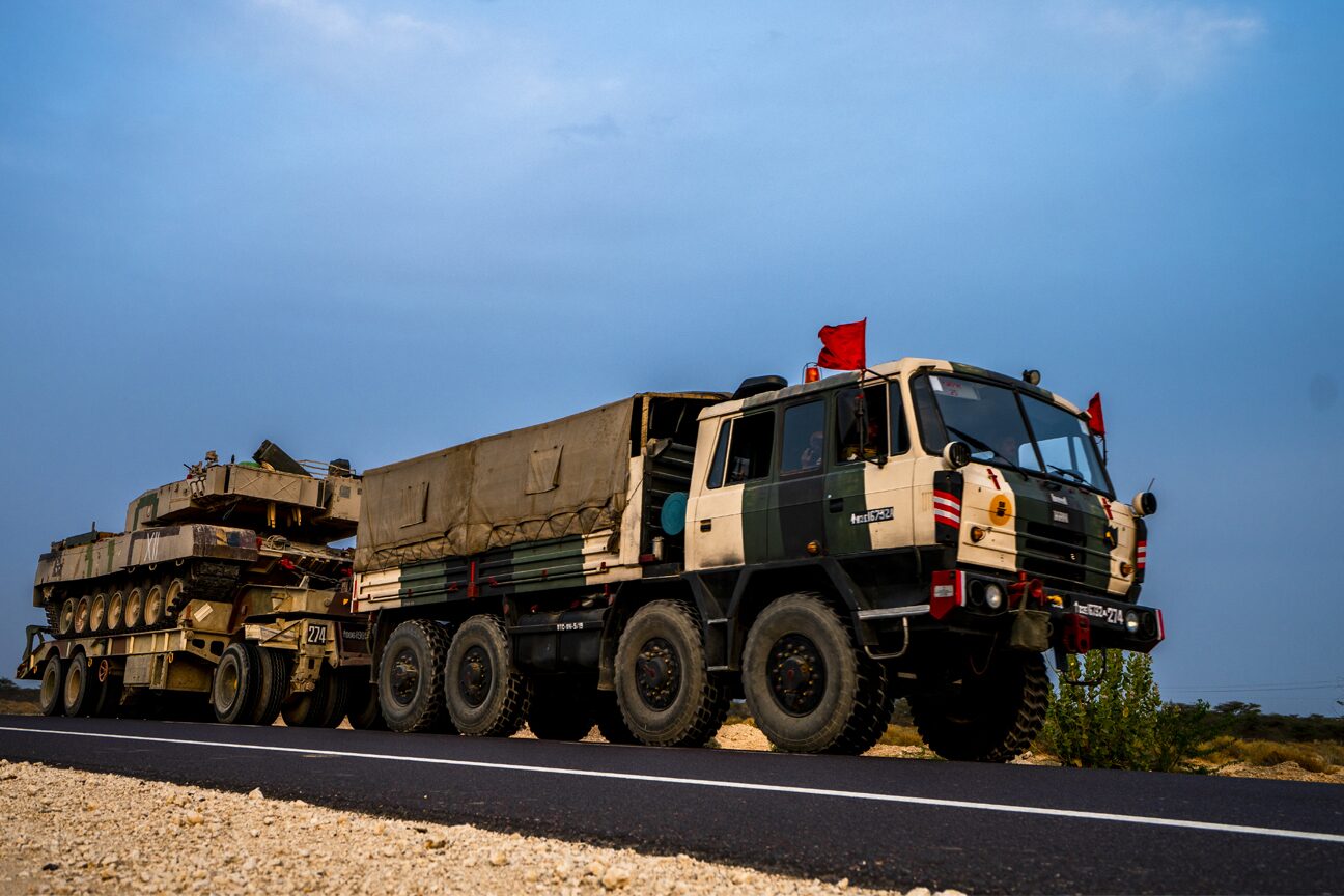 An eight-wheel truck towing a tank on a low-loader trailer at dusk